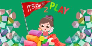 Little Girl PLaing with tows surrounded by bright colored shapes and clay. Flag that says "It's Okay" and text "2 Play"